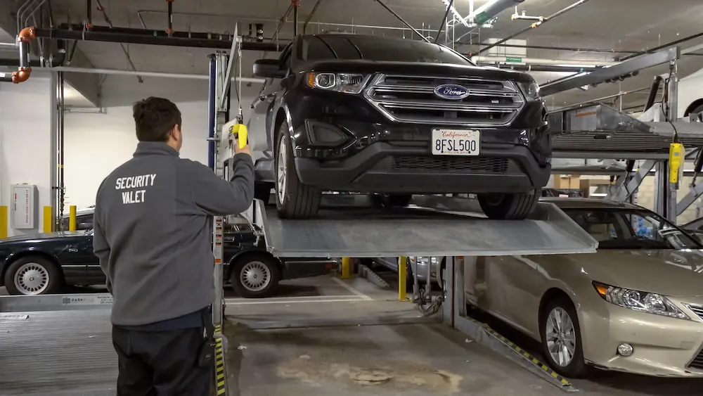 A double-stacker parking lift in operation. The upper platform is mid-cycle with a car loaded, doubling the capacity of a single parking footprint.